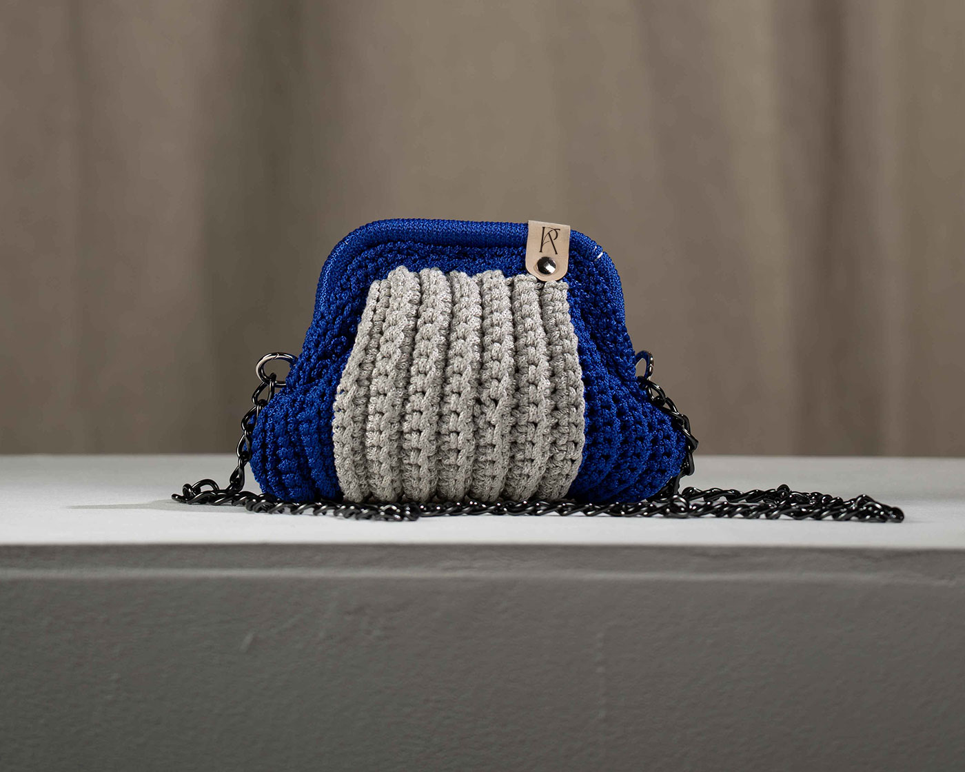 Handcrafted crochet handbag by Rania Kanaki, featuring blue and grey knit textures with metal chain strap